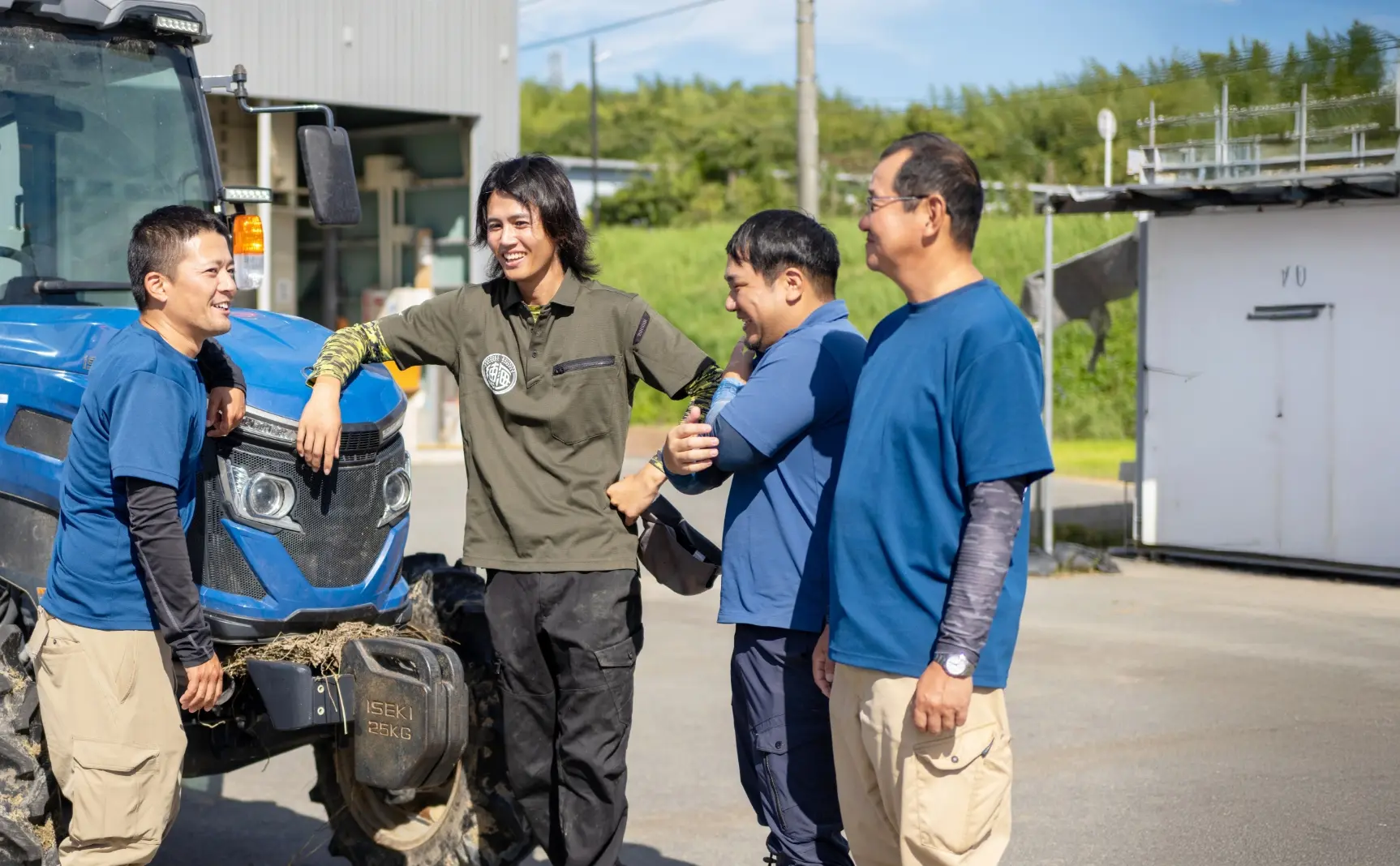 トラクターの前に立ち、笑顔で話している4人のスタッフ