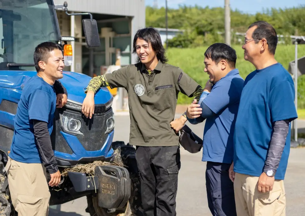 トラクターの前に立ち、笑顔で話している4人のスタッフ